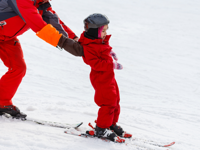 Professional ski instructor is teaching a child to ski on a sunny day on a mountain slope resort