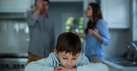 Sad child with arguing parents in the background