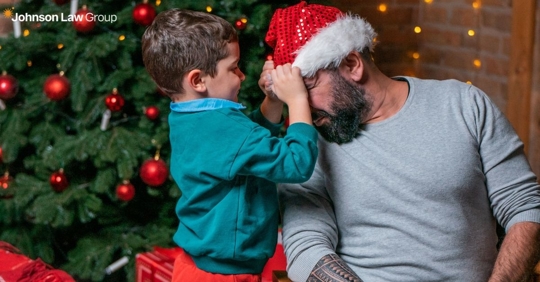 man with a santa hat playing with his child by a christmas tree
