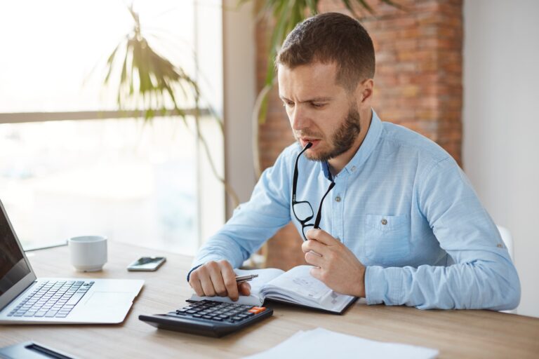 A husband sitting at a table with a calculator and financial documents, representing the financial evaluation and process of computing spousal support obligations.